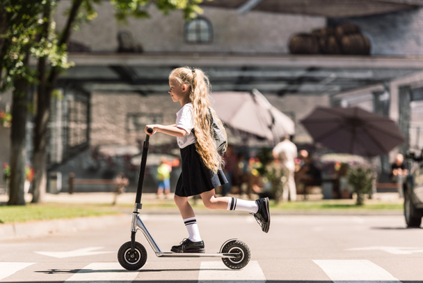vista lateral de lindo niño pequeño con pelo largo rizado montar scooter en la calle
  - Foto, Imagen