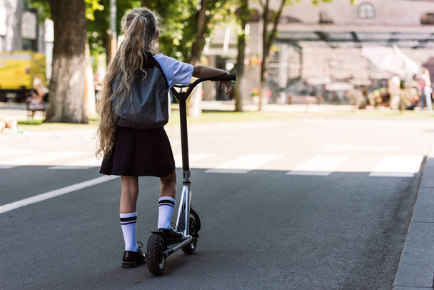 back view of cute little child with backpack riding scooter on street  - Fotografie, Obrázek