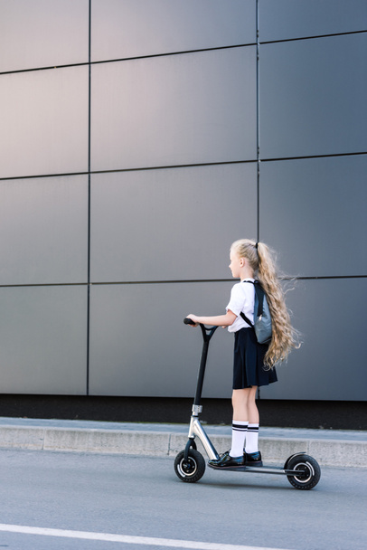 adorable little schoolgirl with long curly hair riding scooter on street  - Φωτογραφία, εικόνα