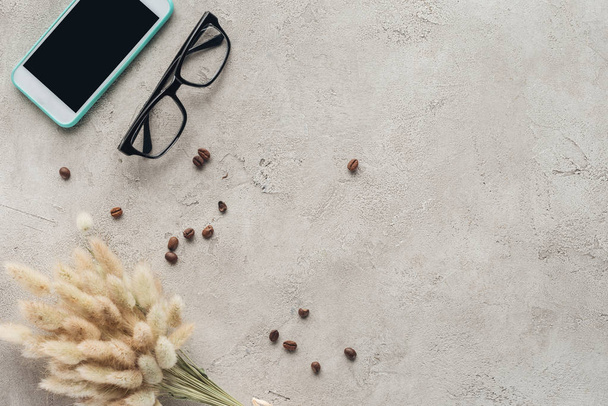 vue du haut du smartphone avec écran vierge avec lunettes, grains de café renversés et bouquet lagurus ovatus sur la surface du béton
 - Photo, image
