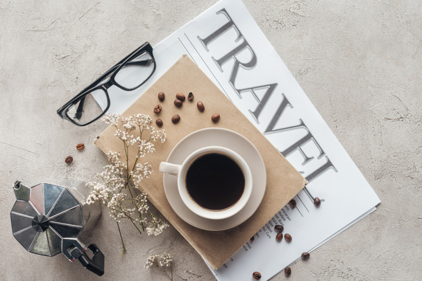 Draufsicht auf köstlichen Kaffee auf Buch und Zeitung mit Reisebeschriftung auf Betonoberfläche - Foto, Bild