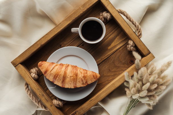 vista dall'alto di caffè e croissant su vassoio con lagurus ovatus bouquet su panno beige, colazione a letto concetto
 - Foto, immagini