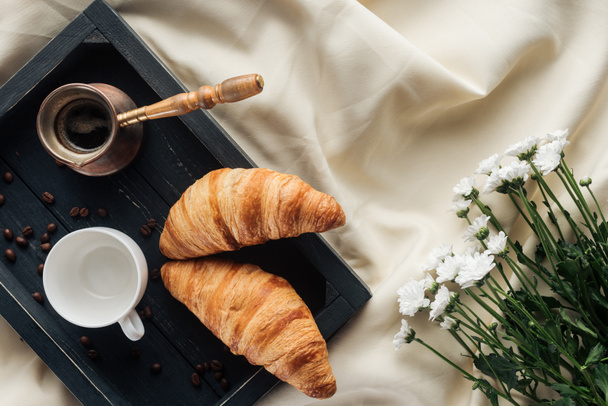 top view of coffee and croissants on tray on beige cloth with field flowers, breakfast in bed concept - Foto, afbeelding