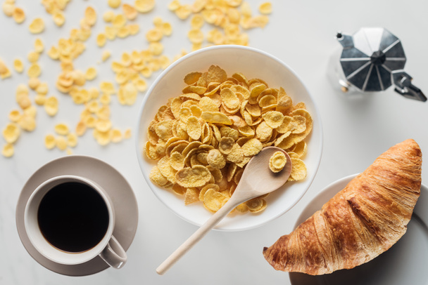 top view of bowl of corn flakes breakfast with cup of coffee and croissant on white - Fotó, kép