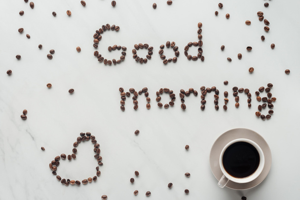vista superior de la taza de café y letras de buenos días hechas de granos de café en mármol blanco
 - Foto, Imagen