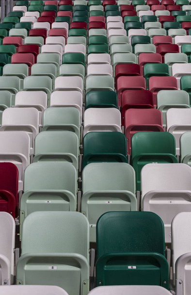Tribunos vazios de um estádio moderno com pepinos sem espectadores e cadeiras coloridas no centro da arena
 - Foto, Imagem