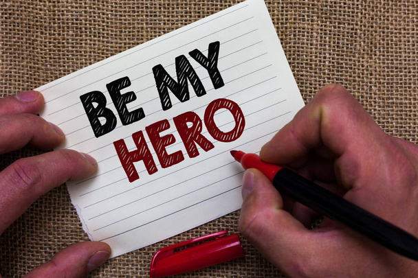 Writing note showing Be My Hero. Business photo showcasing Request by someone to get some efforts of heroic actions for him Man's hand hold white paper with symbolic letter jute sack background - Photo, Image