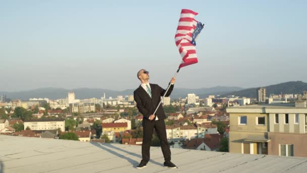 LOW MOTION CLOSE UP: Soddisfatto uomo d'affari di successo e patriota in piedi sulla cima di un alto edificio che detiene la bandiera americana con orgoglio, celebrando il successo e sostenendo patria, nazione, cultura, libertà
 - Filmati, video