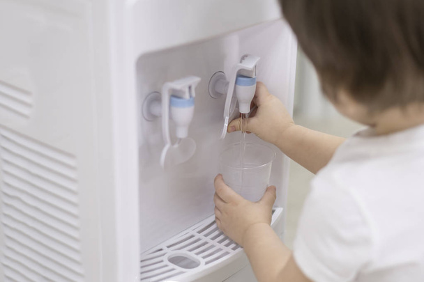 Pequeño niño manos conseguir agua de un refrigerador en una escuela o jardín de infantes
. - Foto, Imagen