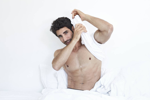 Undressing man in bed, looking to camera - Foto, Bild