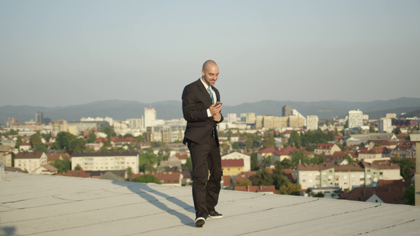Zeitlupe Nahaufnahme dof: aufgeregter Unternehmer, der vor Freude hüpft, als er per Handy die Nachricht vom Abschluss eines Großgeschäfts erhält. Mann jubelt und springt aufs Dach - Filmmaterial, Video