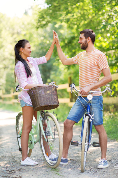 couple with bicycles making high five in summer - Photo, Image