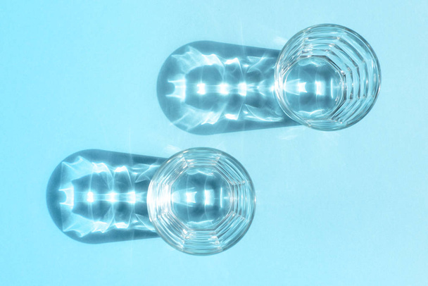 Deux verres en verre transparent sur fond bleu et des ombres d'eux avec des dessins intéressants
 - Photo, image