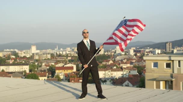 LOW MOTION CLOSE UP: Soddisfatto uomo d'affari di successo e patriota in piedi sulla cima di un alto edificio che detiene la bandiera americana con orgoglio, celebrando il successo e sostenendo patria, nazione, cultura, libertà
 - Filmati, video