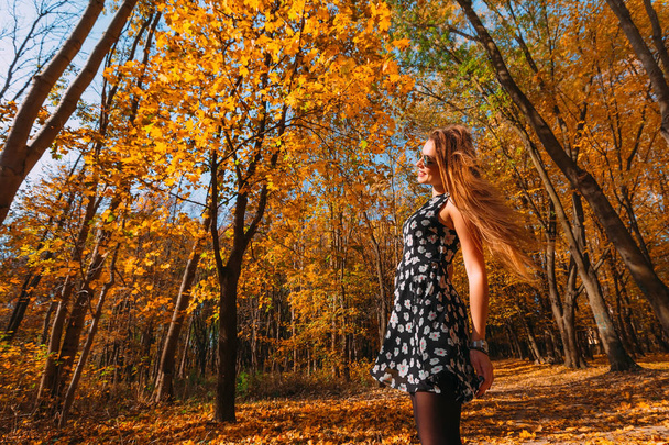 Young beautiful slim teenager girl is joyful spinning and dancing in autumn forest on sunny day. Girl spending time in the autumn park. - Zdjęcie, obraz