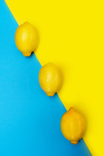 Три жёлтых лимона подряд на жёлто-синем фоне. Вид сверху
. - Фото, изображение