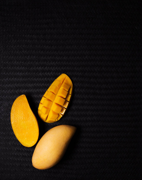 Високий кут зору зображення апетитних фруктів манго з кубиками манго і розрізати половину на фоні текстури чорного плетіння з простором для копіювання
 - Фото, зображення