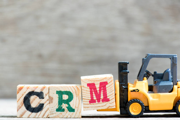 Spielzeuggabelstapler halten Buchstabenblock m in Wort crm (Abkürzung für Customer Relationship Management) auf Holzgrund - Foto, Bild