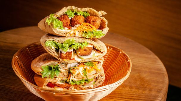 Concept of vegetarian food. pita with falafel, salad, vegetables, tofu cheese in a wicker basket on a wooden table. background image. Copy space, selective focus - Photo, Image