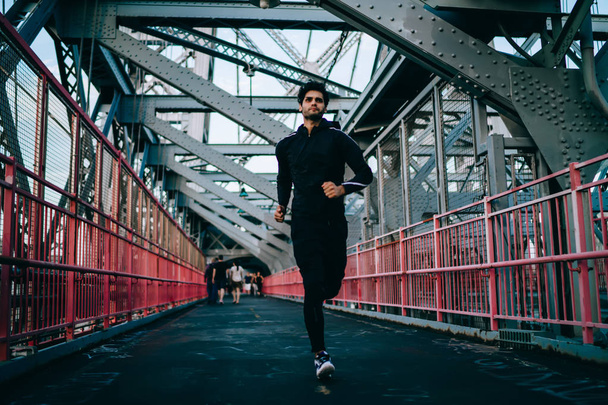 Young male athlete with muscular body practicing sport running for life across modern city bridge, european sportsman enjoying evening jogging and cardio exercises, concept of healthy lifestyle - Foto, Imagen