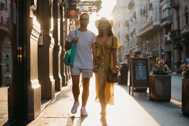 Awesome brunette girl with her boyfriend with beard walking together on the old European street in Spain on the sunset - Photo, Image