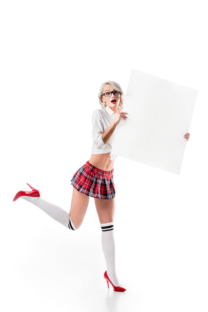 шокированная молодая женщина в униформе колледжа держит пустой баннер изолированный на белом
 - Фото, изображение