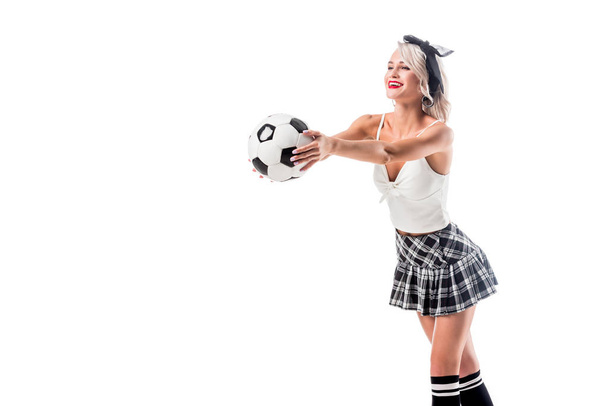 sonriente mujer en seductora falda colegiala a cuadros sosteniendo pelota de fútbol aislado en blanco
 - Foto, imagen