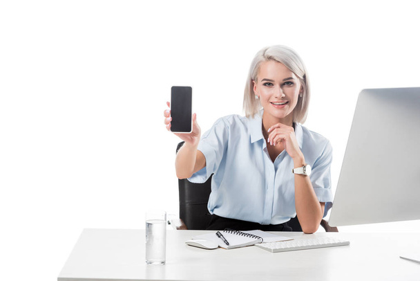 portrait of smiling businesswoman showing smartphone with blank screen at workplace isolated on white - Φωτογραφία, εικόνα