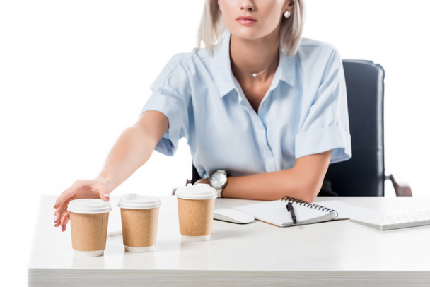 recortado tiro de mujer de negocios en el lugar de trabajo con tazas desechables de café y portátil aislado en blanco
 - Foto, imagen