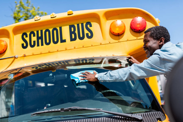 heureux mature afro-américain chauffeur de bus essuyant fenêtre avant de bus scolaire
 - Photo, image