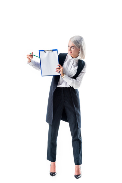 Lächelnde Geschäftsfrau in offizieller Kleidung zeigt auf leeren Notizblock auf weißem Hintergrund - Foto, Bild