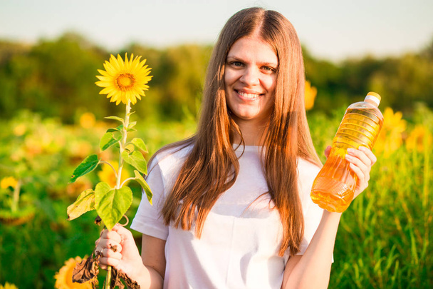 Jonge vrouw in witte bedrijf flesje olie in zonnebloem veld - Foto, afbeelding