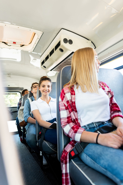 glücklich Teen Schulmädchen Reiten Schulbus mit Klassenkameraden und Blick auf Kamera - Foto, Bild