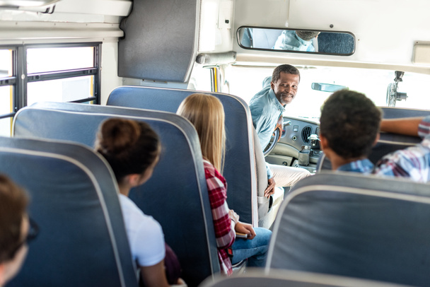 група підлітків, які їдуть на шкільному автобусі і розмовляють з щасливим зрілим водієм
 - Фото, зображення