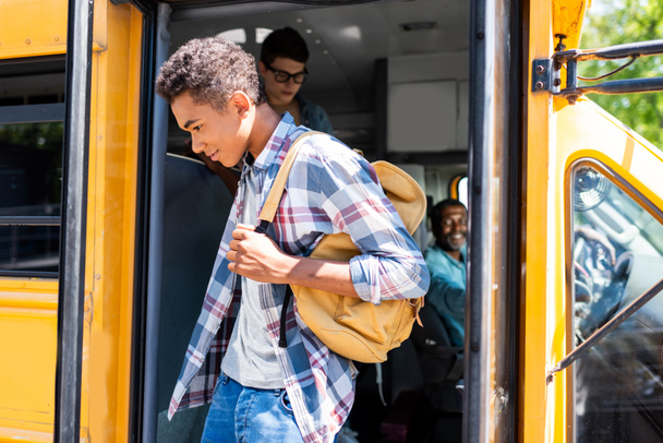Αφρικανική αμερικανική φοιτητής περπάτημα έξω από το σχολικό λεωφορείο ενώ οδηγός τον κοιτάζει - Φωτογραφία, εικόνα