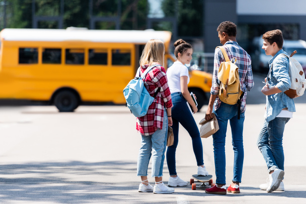 group of teen scholars spending time together on parking in front of school bus - 写真・画像