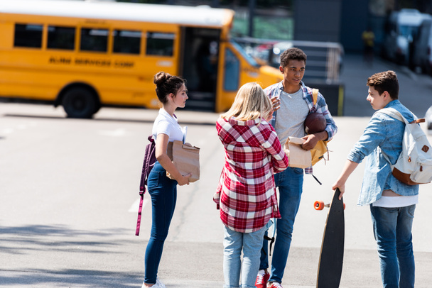 group of teen scholars chatting on parking in front of school bus - Valokuva, kuva
