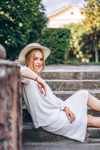 Pretty woman in white vintage dress sitting on stairs outdoor - Fotó, kép