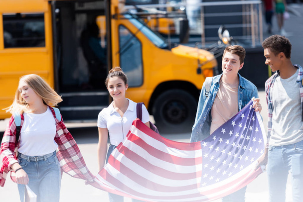group of american teen scholars walking with usa flag in front of school bus - Φωτογραφία, εικόνα