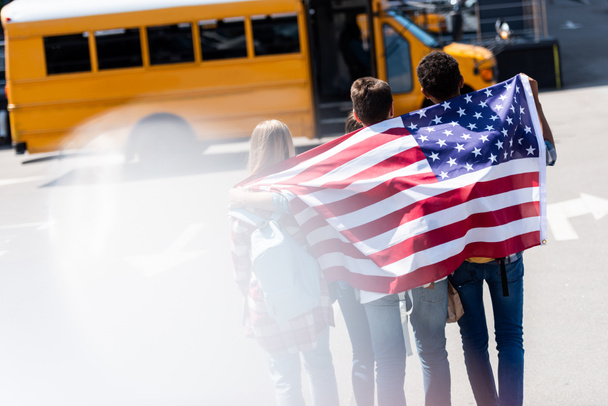 rear view of group of american teen scholars with usa flag in front of school bus - Photo, Image
