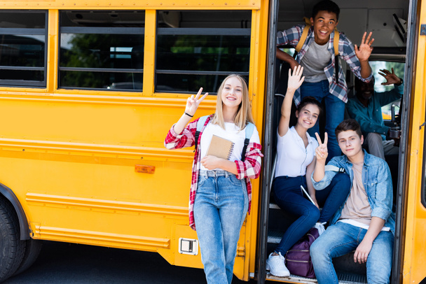 Gruppe von Teenagern sitzt am Schulbus mit Fahrer drinnen und zeigt verschiedene Gesten in die Kamera - Foto, Bild