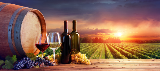 Бутылки и бокалы с виноградом и бочкой в сельской местности
 - Фото, изображение