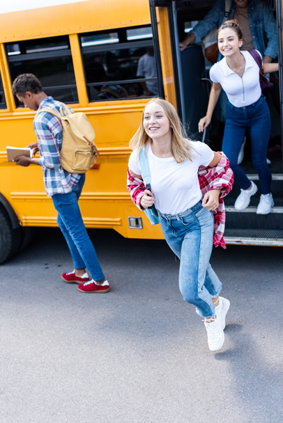 smiling multiethnic teen scholars running out school bus  - Photo, Image
