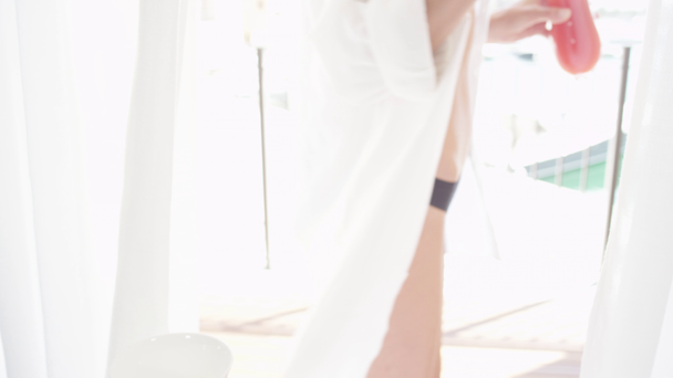 LENTA MOCIÓN CERRAR DOF: Mujer joven caucásica en camisa blanca recogiendo jugo de fruta recién exprimido para el desayuno en la impresionante habitación de hotel de lujo e ir a la terraza con vista al puerto de velero
 - Imágenes, Vídeo