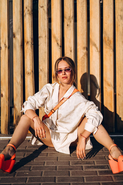 Fashionable woman sitting on street near wooden fence - Foto, Imagen