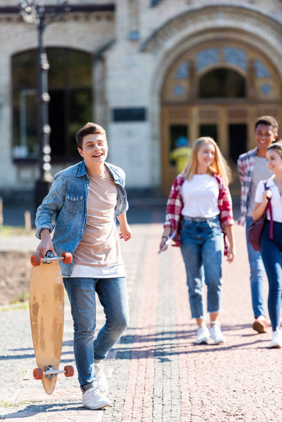 happy teen schoolboy with skateboard walking with friends after school - Foto, imagen