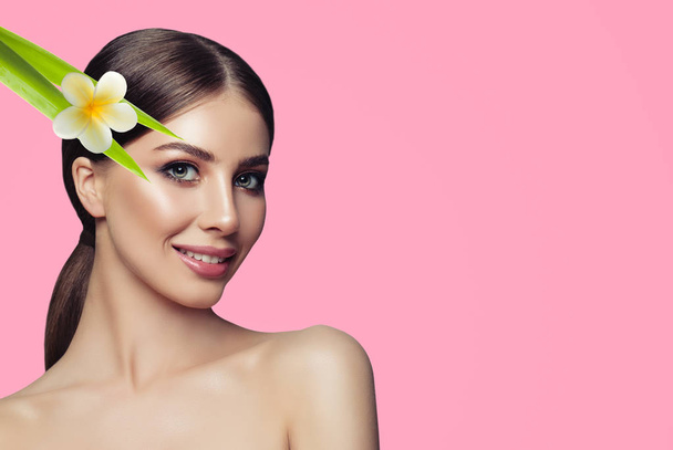 Beautiful young woman with clean perfect skin. Beauty model with natural makeup, flower and green leaves. Spa, skincare and wellness concept - Fotoğraf, Görsel