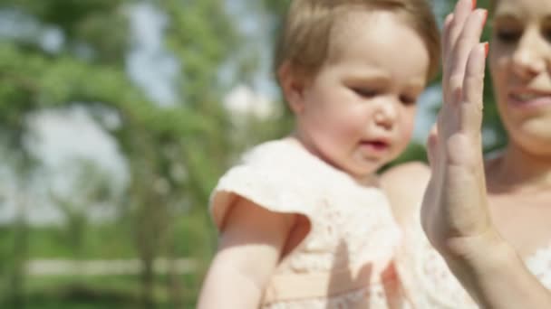 Slow Motion Close Up, Dof: Docela mladá maminka držela malou dceru v náručí. Bezstarostné dítě hrát si s rodiči, dávat vysoké pět a tleskání rukama v místním parku na slunečný letní den - Záběry, video