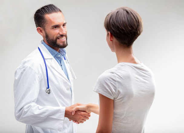 Hymyilevä mieslääkäri kättelee naispotilasta olkanäkymässä valkoisella
 - Valokuva, kuva