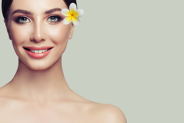 Spa kadın yüzü. Sağlıklı cilt, sevimli gülümseme ve arka plan üzerinde tropikal çiçek güzel kadın modeli - Fotoğraf, Görsel